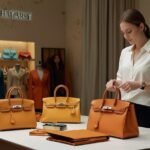 An American customer personalizes a Hermès Birkin bag with custom embroidery at a Paris boutique, driven by 2025 US tariffs on luxury goods.